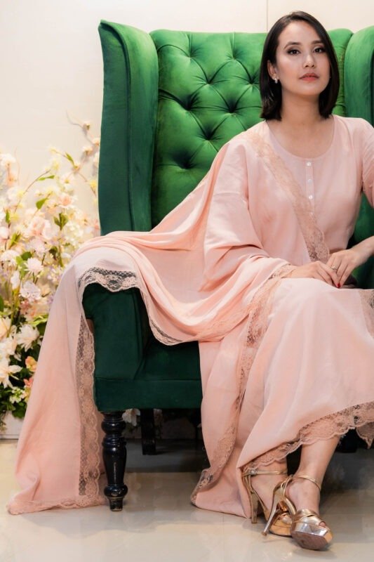 Model seated on tufted armchair wearing Blush Raag kurti with lace-trimmed dupatta