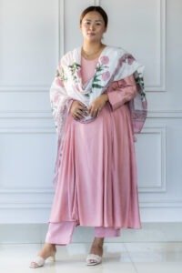 Woman wearing blush pink kurti with white floral dupatta, standing against white paneled wall