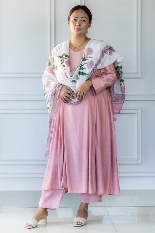 Woman wearing blush pink kurti with white floral dupatta, standing against white paneled wall