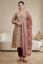 Person wearing a beige kurta with maroon and green floral prints, paired with maroon pants and matching dupatta with circular motifs and floral border, accessorized with silver jewelry.