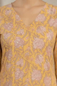 Close-up of a mustard yellow garment with a V-neckline, showcasing an intricate floral print in light pink and beige with repeating flowers and leaves.
