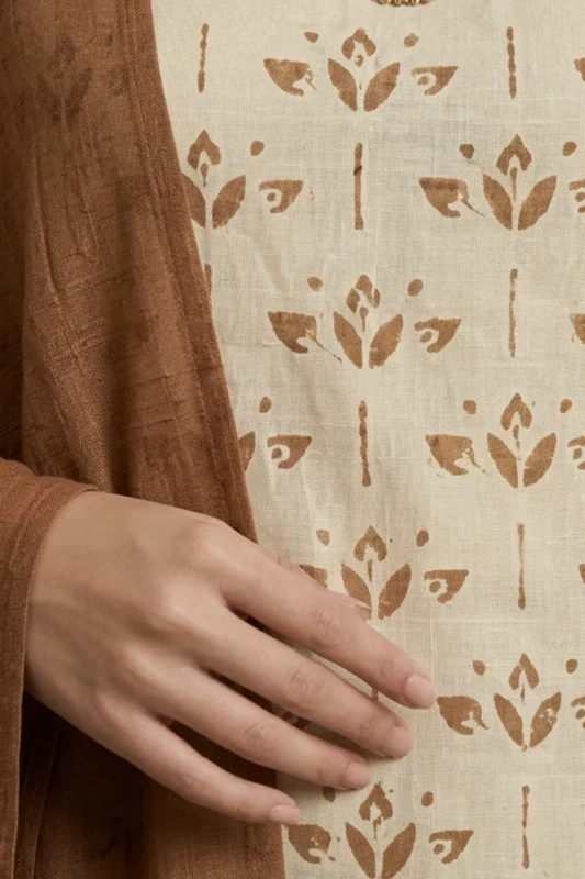 Close-up of a hand resting on beige fabric featuring a repeating brown floral pattern, partially covered by a textured brown garment.
