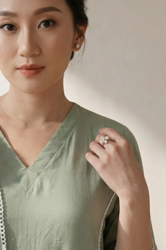 Close-up of a woman wearing the Nazm V-neck olive green kurti, showcasing the clean V-shaped neckline and delicate white lace trim details paired with pearl jewelry.