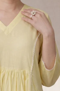 A detailed close-up of the Canvas Kurti V Neck in a soft lemon yellow, highlighting the clean V-shaped neckline and vertical white lace trim detailing on the bodice.