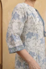 A close-up of the Urban Utopia kurta sleeve, highlighting the breathable Kota Doria texture. The three-quarter sleeve finishes with a decorative blue floral border. The image also shows the delicate white ladder lace running down the side of the garment, emphasizing the handmade quality.