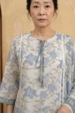 Detailed view of the Urban Utopia kurta neckline. The white Kota Doria fabric shows its characteristic square-check weave, adorned with blue floral patterns. The round neckline features a keyhole opening secured by blue braided tassels. Vertical white lace inserts add a refined structural detail to the bodice.