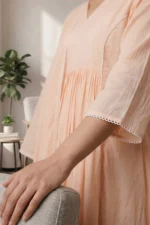 A detailed close-up of the ORA Ethnic V Neck peach kurti, showing the breathable fabric, gathered waistline, and delicate white lace trim on the sleeve cuffs.