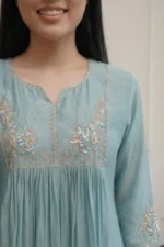 A detailed close-up of the yoke and neckline of the seafoam blue Majuli Muse kurti. The image highlights the intricate silver thread embroidery and delicate sequin work in floral and paisley patterns. The fabric has a subtle sheen, and the craftsmanship of the hand-worked details is clearly visible.