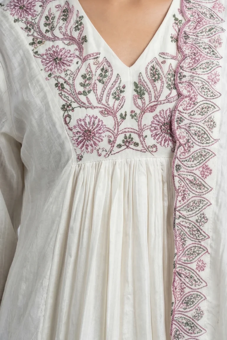 Close‑up of Althea Mul Cotton Luxe Kurti in white cotton with pink and green floral embroidery, V‑neckline, and scalloped edge detailing.