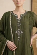 A detailed close-up of the chest area of a red kurti, showcasing precise vertical pintuck pleats and delicate white floral embroidery on the sides. The neckline features a round collar and a central fabric button detail.
