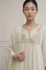 A detailed close-up shot of the white kurti's chest area, showcasing dense hand-embroidered floral patterns in matching white thread. The design includes delicate gathers below the embroidery, creating a graceful, voluminous flared fit.