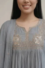 A detailed close-up of the teal kurti's chest area, showcasing a U-shaped hand-embroidered floral pattern in contrasting white and lighter teal threads. Soft gathers below the embroidery add volume to the flared design.