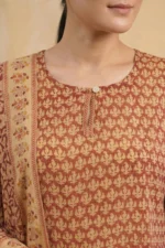 A close-up view of the Nysa kurta’s bodice. The design shows a simple round neckline with a small keyhole opening and a single white button. The rust-colored Kota Doria fabric displays a repeating hand-block motif in a lighter cream shade. A portion of the matching dupatta with a floral border is draped over the shoulder.