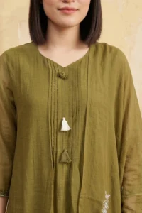 Close-up of an olive green kurti featuring vertical pintuck pleats on the chest. The neckline is adorned with a fabric-covered knot button and two decorative hanging tassels in white and green.