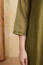 Detailed shot of the three-quarter length sleeve of the olive green kurti. The cuff features a fine embroidered border of tiny green flowers and a delicate white running stitch along the edge.