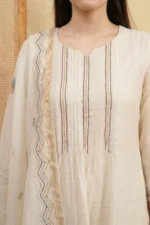 A detailed close-up shot focusing on the kurti's bodice, showcasing precise vertical pintuck pleats and handcrafted decorative tassels at the neckline. Intricate white floral thread-work is visible on the shoulders.