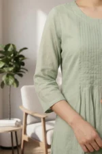 A lifestyle image of the Nazm sage green set featuring the flowing dupatta with delicate floral lace borders. The outfit is styled for a minimal, elegant aesthetic in a naturally lit setting.