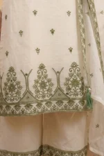 A detailed shot highlighting the craftsmanship of the StyleMélange set. The bottom of the natural-toned kurta features a large, ornate scalloped embroidery pattern in olive green, accented with tiny mirrors that catch the light. Below, the wide-leg palazzos show a coordinating olive embroidered border, maintaining a cohesive and sophisticated aesthetic.
