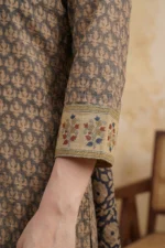 A close-up view of the Veda Wear kurta's upper bodice. The design shows a simple round neckline with a small white button detail and a narrow vertical slit. A dupatta with an intricate floral border in yellow, red, and blue is draped over the shoulder, contrasting with the subtle patterns of the Kota Doria fabric.
