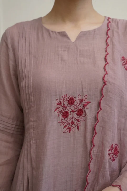 A detailed macro shot of the kurti's bodice, showcasing precise vertical pintuck pleats and handcrafted decorative tassels hanging from the neckline. The intricate thread-work embroidery is visible along the shoulders.