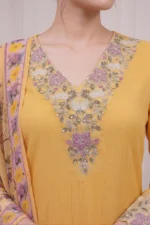 Close-up of the Marigold Kurti's V-neckline, showcasing ornate floral embroidery in pink, olive green, and silver threads with subtle sequin embellishments on textured yellow fabric.