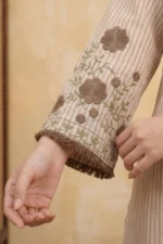 Close-up of the Mocha Bloom Kurta Set showing a bell sleeve with brown and sage green floral and vine threadwork embroidery on a pink striped cotton fabric with a decorative brown fringe trim at the hem