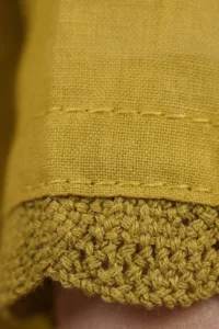 Close-up of the Mustard Vine Kurta Set showing a textured crochet border trim at the hem with fine hand-stitched detailing on olive yellow cotton fabric