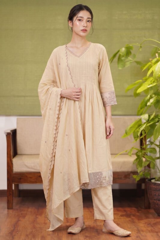 Full body view of a model wearing The Dune Kurti, a natural kora beige ethnic suit set featuring a pintuck bodice, matching trousers, and a scalloped dupatta.
