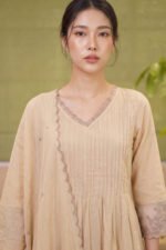 Close-up front view of The Dune Kurti in natural kora beige, highlighting the V-neckline with scalloped lace trim and delicate pintuck pleating across the chest.