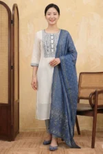 A woman wearing the White Indigo Kurta Set comprising a straight-cut white textured check kurta with navy blue embroidered yoke and cuff details, matching blue printed straight-leg pants, and a blue floral printed dupatta, styled with blue juttis