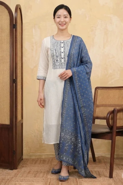 A woman wearing the White Indigo Kurta Set comprising a straight-cut white textured check kurta with navy blue embroidered yoke and cuff details, matching blue printed straight-leg pants, and a blue floral printed dupatta, styled with blue juttis