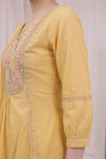 Close-up of the Yellow Garden Kurta Set showing a richly embroidered square yoke with pink and sage green floral threadwork, mirror work border and gold embroidered placket trim on soft yellow cotton fabric with a gathered waist and elasticated three-quarter sleeve cuff