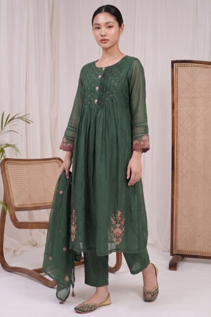 Full-length view of the Verdant Flora Kurti set in deep green, featuring a pintucked yoke, matching trousers, and a dupatta, styled in a warm minimalist setting.