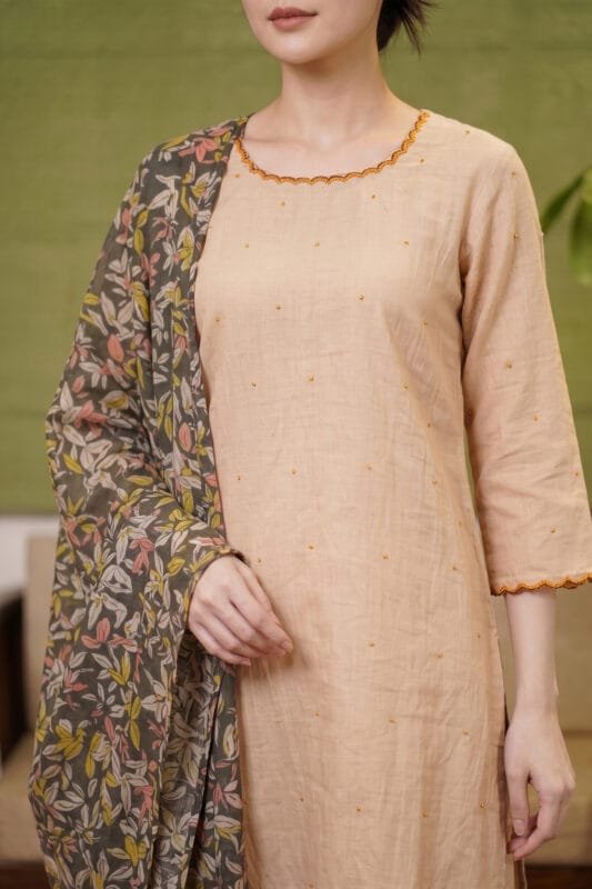 Close-up of the Sand Dot Kurti showcasing the round neckline with contrasting scalloped edging, precise yoke alignment, scattered embroidered dot motifs on the bodice, and a dark floral dupatta draped over the shoulder.