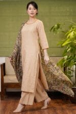 Full-length view of a model walking in the beige Sand Dot Kurti set, featuring a straight-cut silhouette with small dot motifs, matching wide-leg trousers with scalloped hems, and a dark, flowing floral printed dupatta.
