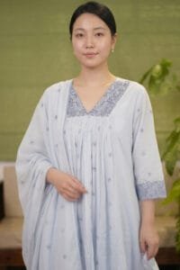 Close-up front view of the dusty blue Blossom Blue Chanderi Kurti Set, focusing on the precise technical construction of the V-neckline and the heavily embroidered yoke. The image showcases the accurate pleat alignment cascading down the front and the delicately scalloped border of the draped dupatta.