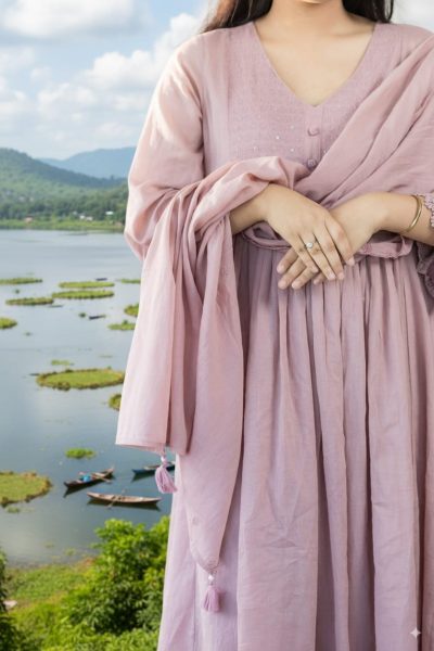 A woman wearing a pastel pink embroidered kurti with dupatta, standing near Loktak Lake in Manipur, representing elegant ethnic fashion.